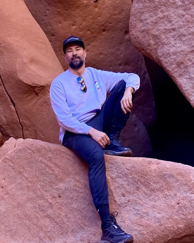 Jacob Ando smiling, seated on a boulder in a red sandstone canyon